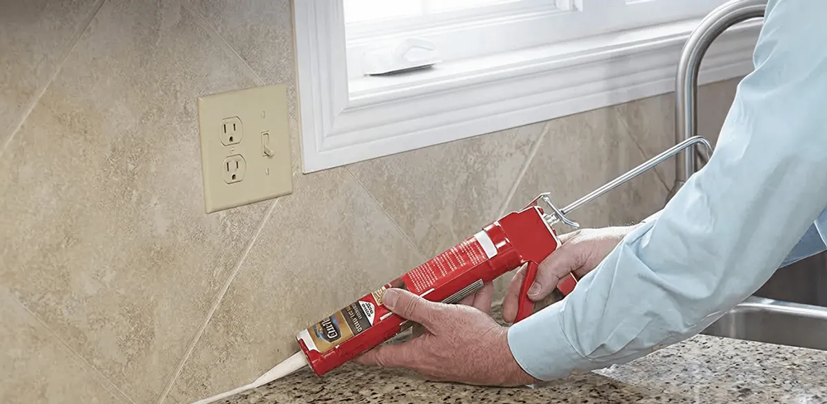 Handyman applying caulk along a kitchen backsplash and countertop seam in Kansas City, KS