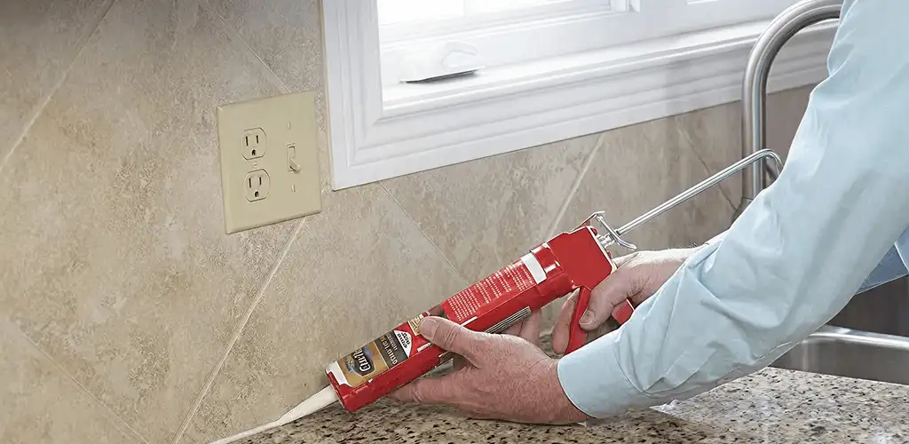 Handyman applying caulk along a kitchen backsplash and countertop seam in Kansas City, KS