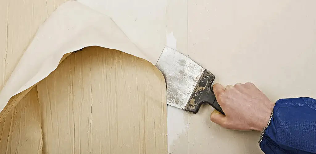 Handyman removing wallpaper with a scraper for wall preparation in Kansas City, KS